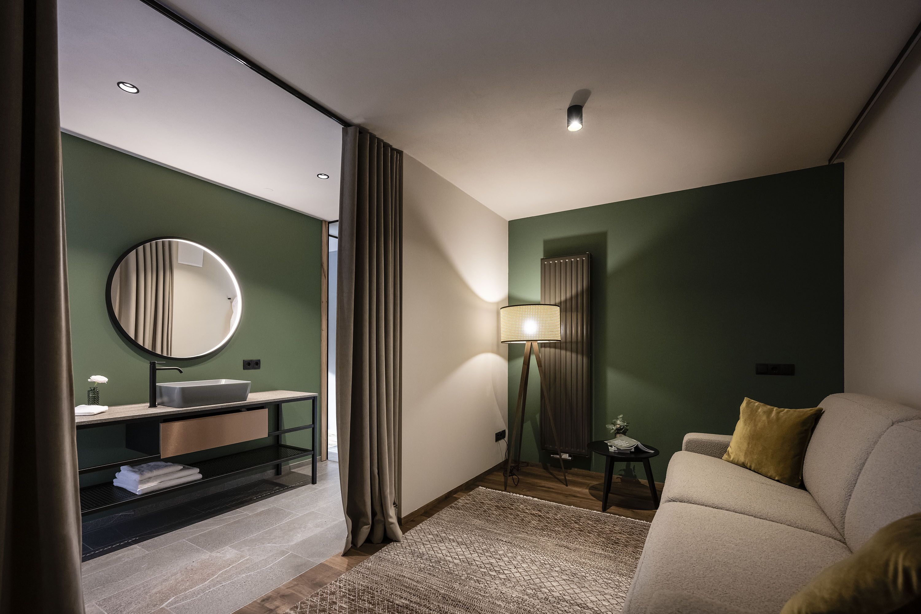 Une chambre d’hôtel moderne avec un miroir rond, un lavabo, un canapé et une lampe.