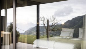Een slaapkamer met een groot bed, uitzicht op bergen en een glazen deur naar een terras.