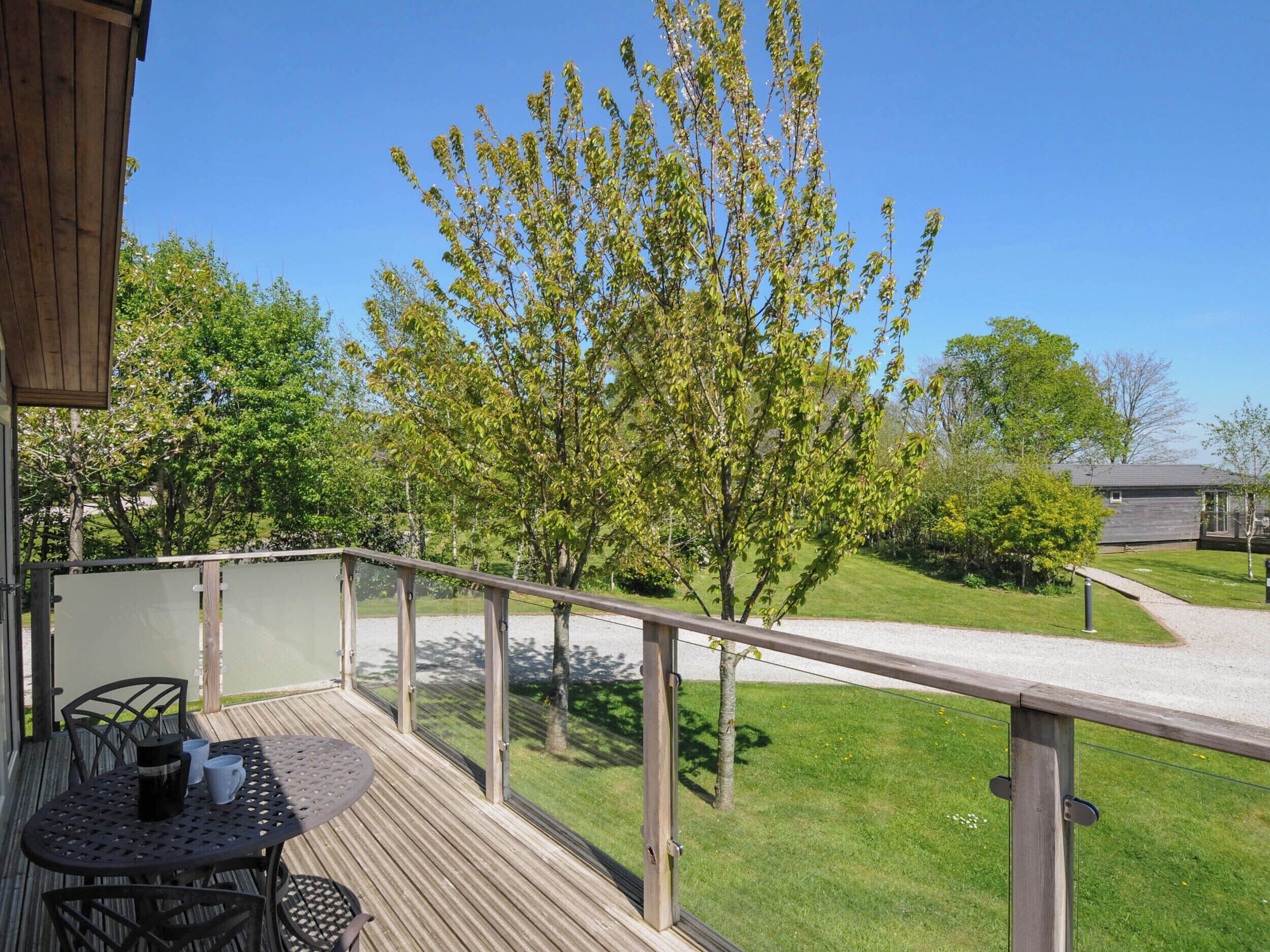 Eine Holzterrasse mit Tisch und Stühlen, mit Blick auf eine Rasenfläche mit Bäumen und einem Gebäude im Hintergrund.