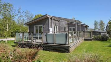 Una cabaña moderna con terraza, rodeada de césped cuidado y vegetación natural.