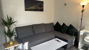 A modern living room with a grey sofa, a small white table, and a potted plant. - Cosy Stay In Birmingham by Villazu (Birmingham)