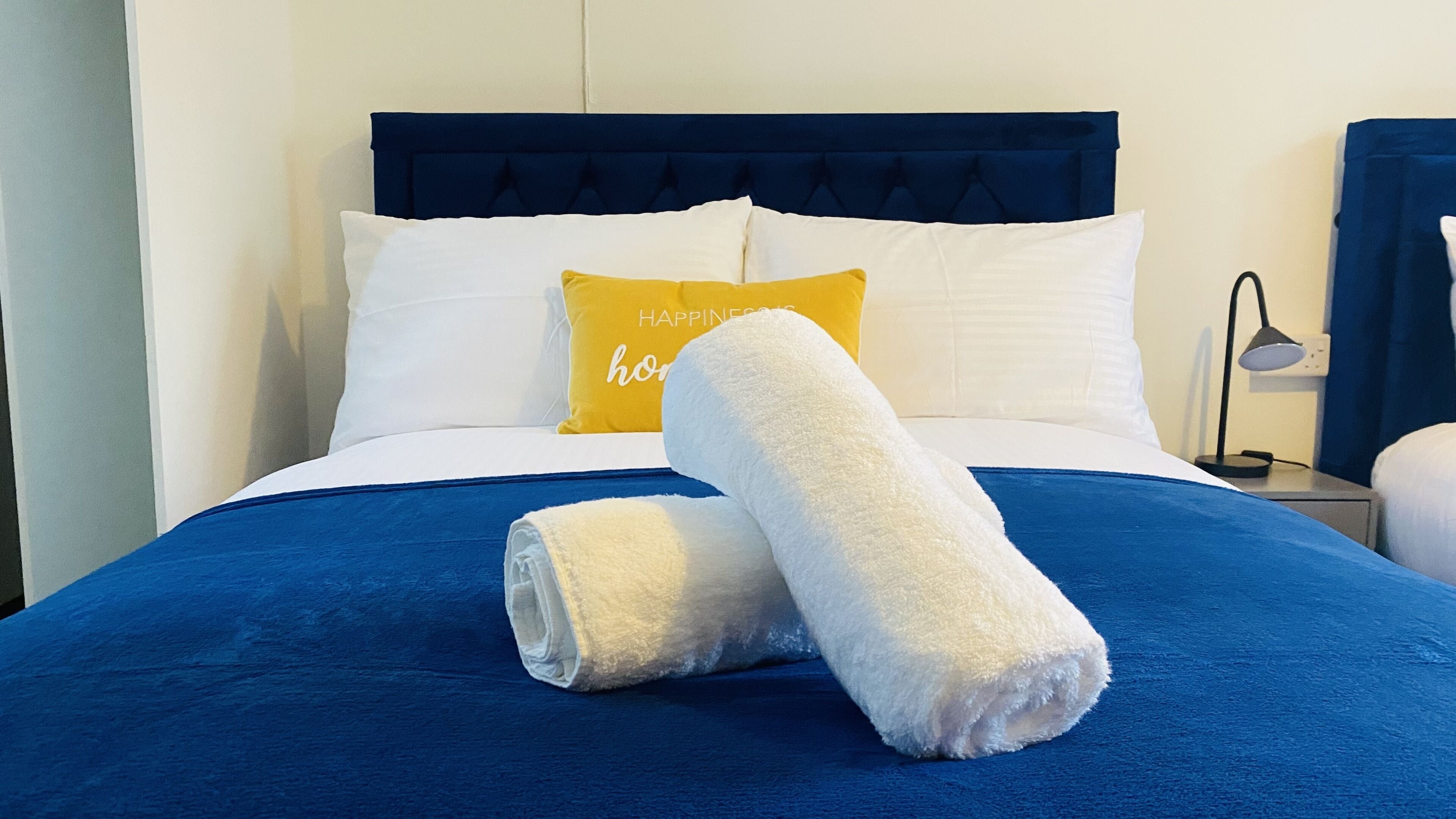 A neatly made bed with a blue bedspread, white pillows, and a yellow pillow with text.