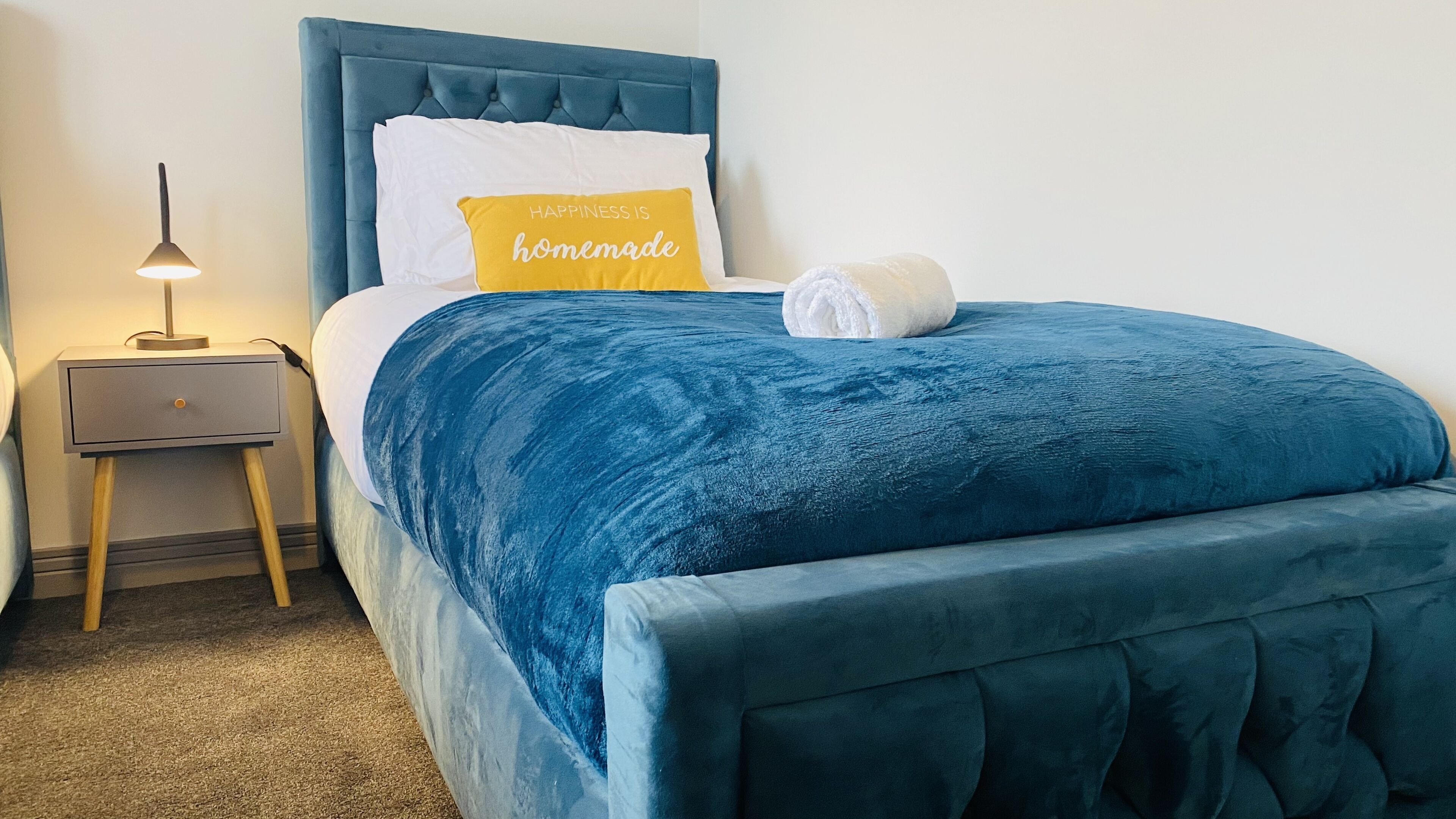 Una cama bien hecha con un cabecero azul y un almohadón blanco con uno amarillo encima.