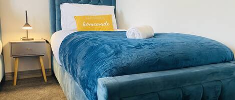 A neatly made bed with a blue headboard and a single white pillow with a yellow pillow on top.