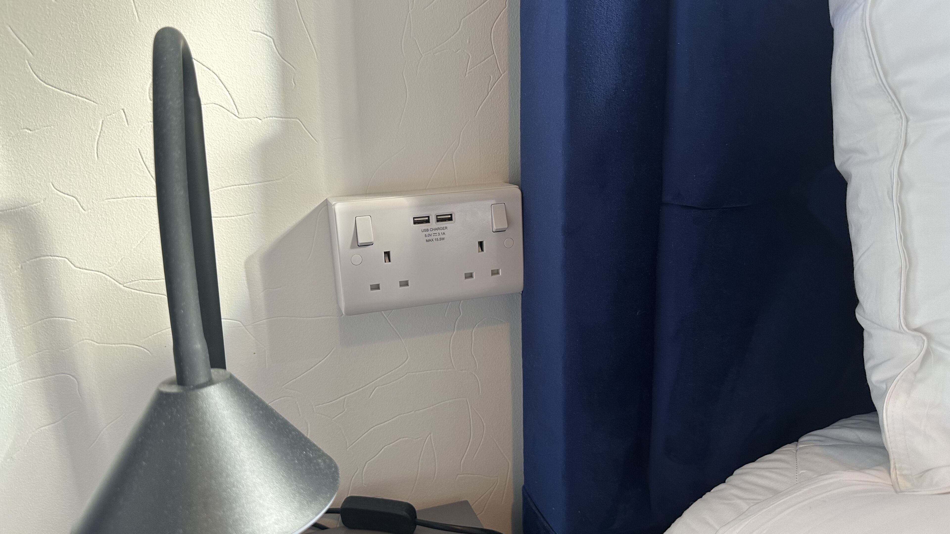 A power outlet with a USB charger, a lamp, and a blue curtain.