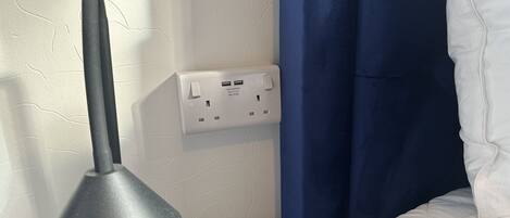 A power outlet with a USB charger, a lamp, and a blue curtain.