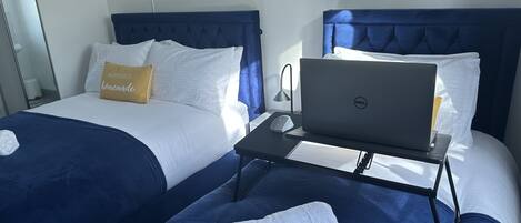 A hotel room with two beds, a laptop on a small table, and a towel on the bed.