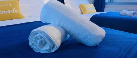 Una cama bien tendida con ropa de cama azul y dos toallas blancas enrolladas.