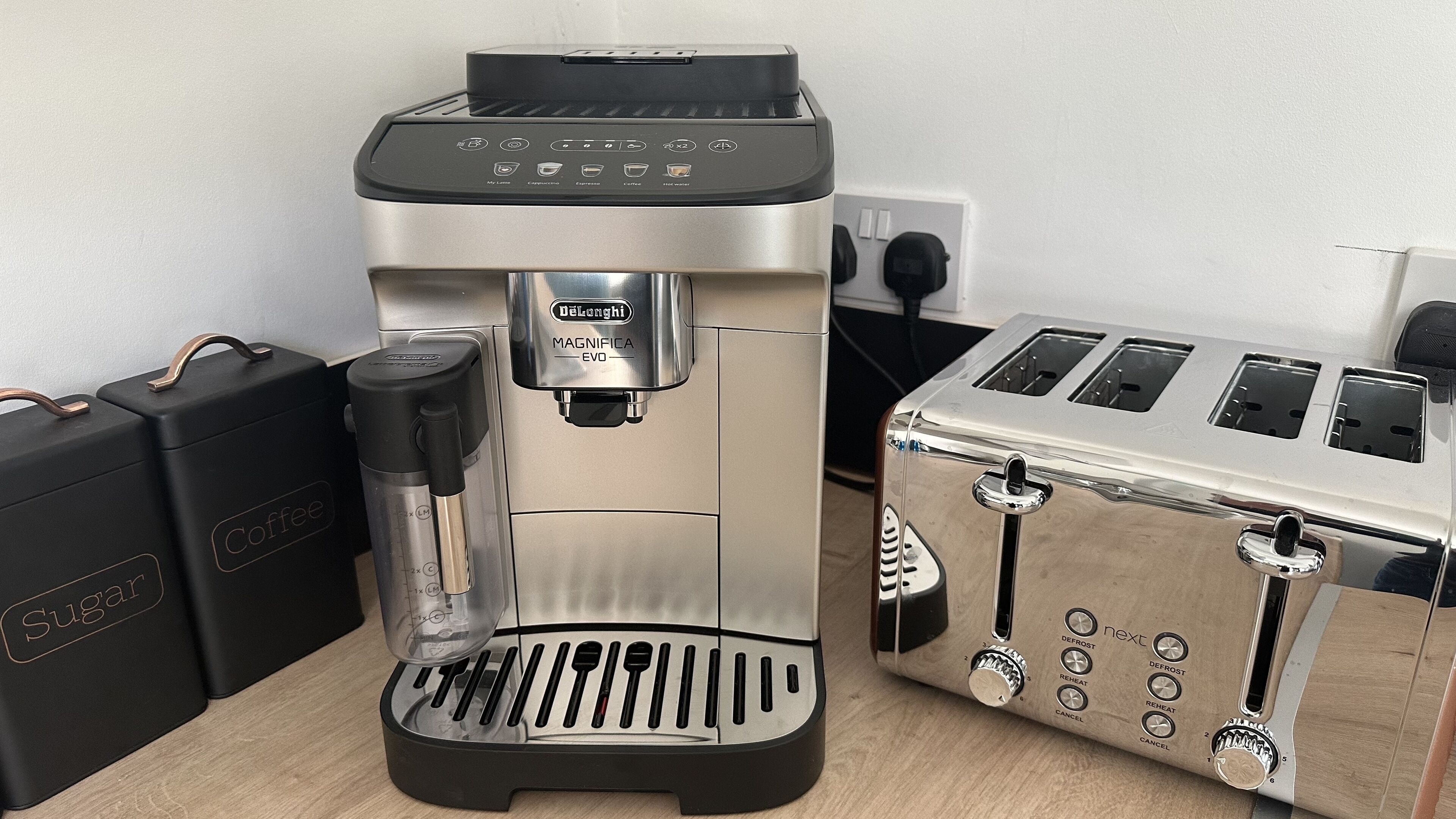 A coffee machine with a milk frother, a toaster, and two containers labeled "Sugar" and "Coffee".