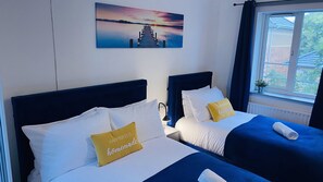 A hotel room with two beds, each with white bedding and a blue headboard. There is a painting of a sunset on the wall above the beds. - Cosy Stay In Birmingham by Villazu (Birmingham)