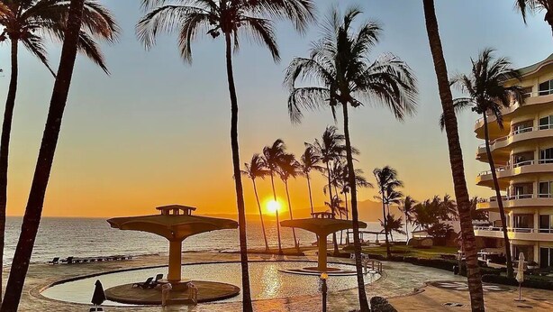 Ein Resort mit Palmen, einem Poolbereich und Blick auf den Sonnenuntergang.