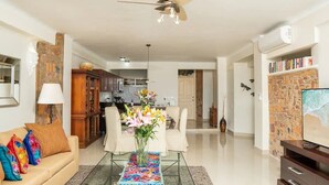 Ein geräumiges Wohnzimmer mit einer Couch, einem Couchtisch mit Blumenvase, einem Deckenventilator und einem Fernseher auf einem Holzboden.