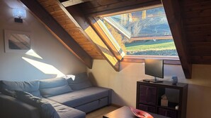 Una habitación acogedora con techo inclinado, un sofá, una mesa y un televisor.