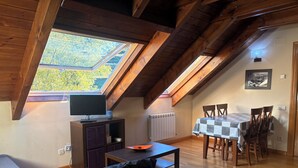 Un espacio tipo loft con techo de madera, una mesa de comedor con sillas, un sofá y un televisor sobre un mueble.