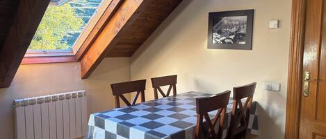 Un comedor con mantel a cuadros, sillas de madera, un radiador, un cuadro enmarco y una puerta de madera.