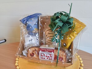 Un panier-cadeau contenant divers articles, notamment un gâteau, un sac bleu et un sac jaune, le tout emballé dans du plastique transparent et décoré de rubans.