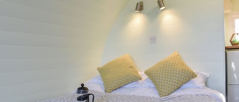 A neatly made bed with a patterned blanket, two pillows, a book, and a coffee maker on the side.