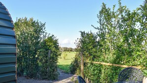 A patio area with a gravel path, metal table and chairs, and a view of a green field and trees. - Privet Pod - UK41394 (Lathom, near Southport)