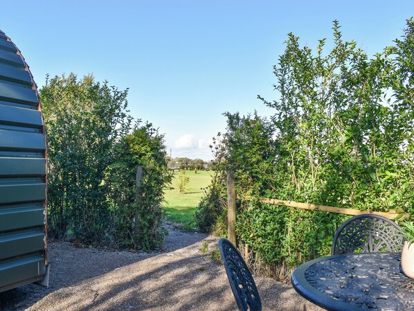 A patio area with a gravel path, metal table and chairs, and a view of a green field and trees.