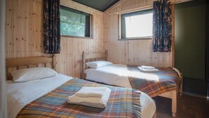 Une chambre avec trois lits en bois, chacun recouvert d’une couverture à carreaux et agrémenté d’oreillers blancs.