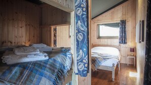 Une cabine avec deux lits en bois, une fenêtre avec des rideaux et une petite table avec une lampe.