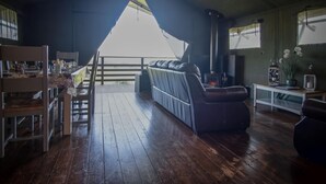 Un salon chaleureux avec un plancher en bois, un canapé, une table avec une lampe et une vue sur l’extérieur.