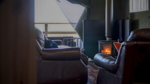 Une pièce chaleureuse avec une cheminée, des fauteuils en cuir et une vue sur l’extérieur.