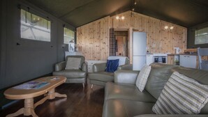 Una sala de estar acogedora con un sofá, sillones y una mesa de madera. Se observa una cocina al fondo.
