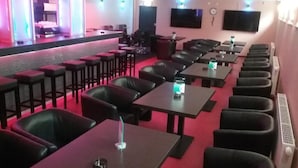 A restaurant with multiple tables and chairs, a bar area with stools, and a flat-screen TV mounted on the wall. - P&P V-V UG (Stuttgart)