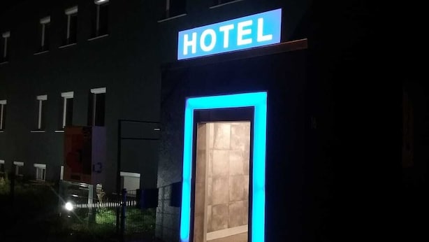 A hotel entrance with a neon sign, a visible door, and a small window. - P&P V-V UG (Stuttgart)