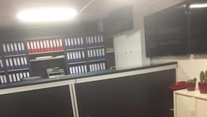 A room with a black leather couch, a red carpet, a desk with a computer, and a cabinet with plants. - P&P V-V UG (Stuttgart)