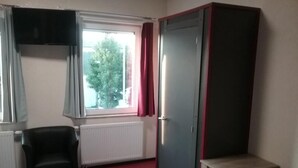 A room with a window, a radiator, a black chair, a wardrobe, and a small table. - P&P V-V UG (Stuttgart)