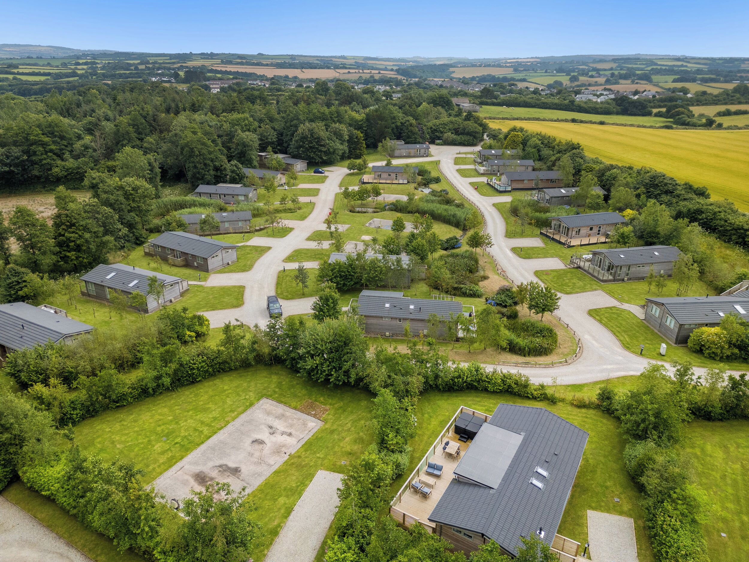 Eine Vogelperspektive zeigt eine Wohngegend, in der Häuser kreisförmig um eine zentrale Straße angeordnet sind, umgeben von grünen Feldern und Bäumen.