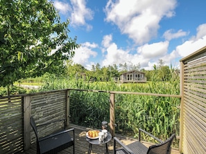 Eine Holzdiele mit Tisch und Stühlen, mit Blick auf einen Garten mit hohen Pflanzen und einem Haus im Hintergrund.