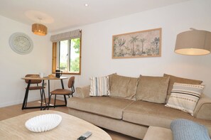 Ein Wohnzimmer mit Sofa, Couchtisch, Esstisch mit Stühlen, einer Uhr, einem Fenster mit Vorhängen, einem Gemälde und einer Lampe.