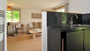 A modern kitchen with a black countertop, stainless steel sink, and a dining area with a wooden table and chairs. - 12 Meadow Retreat (Liskeard)