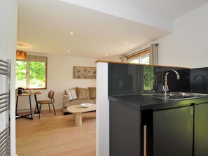 A modern kitchen with a black countertop, stainless steel sink, and a dining area with a wooden table and chairs. - 12 Meadow Retreat (Liskeard)