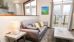 En moderne stue med en grå sofa, et lille bord med en lampe og udsigt til en have gennem en skydedør.