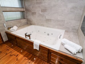 A modern bathroom with a large bathtub, wooden vanity, and a window with blinds.