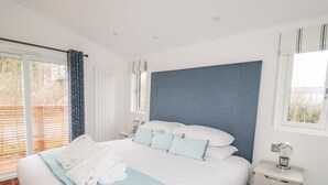 A modern bedroom with a large bed, a bedside table, a nightstand, and a window with curtains.