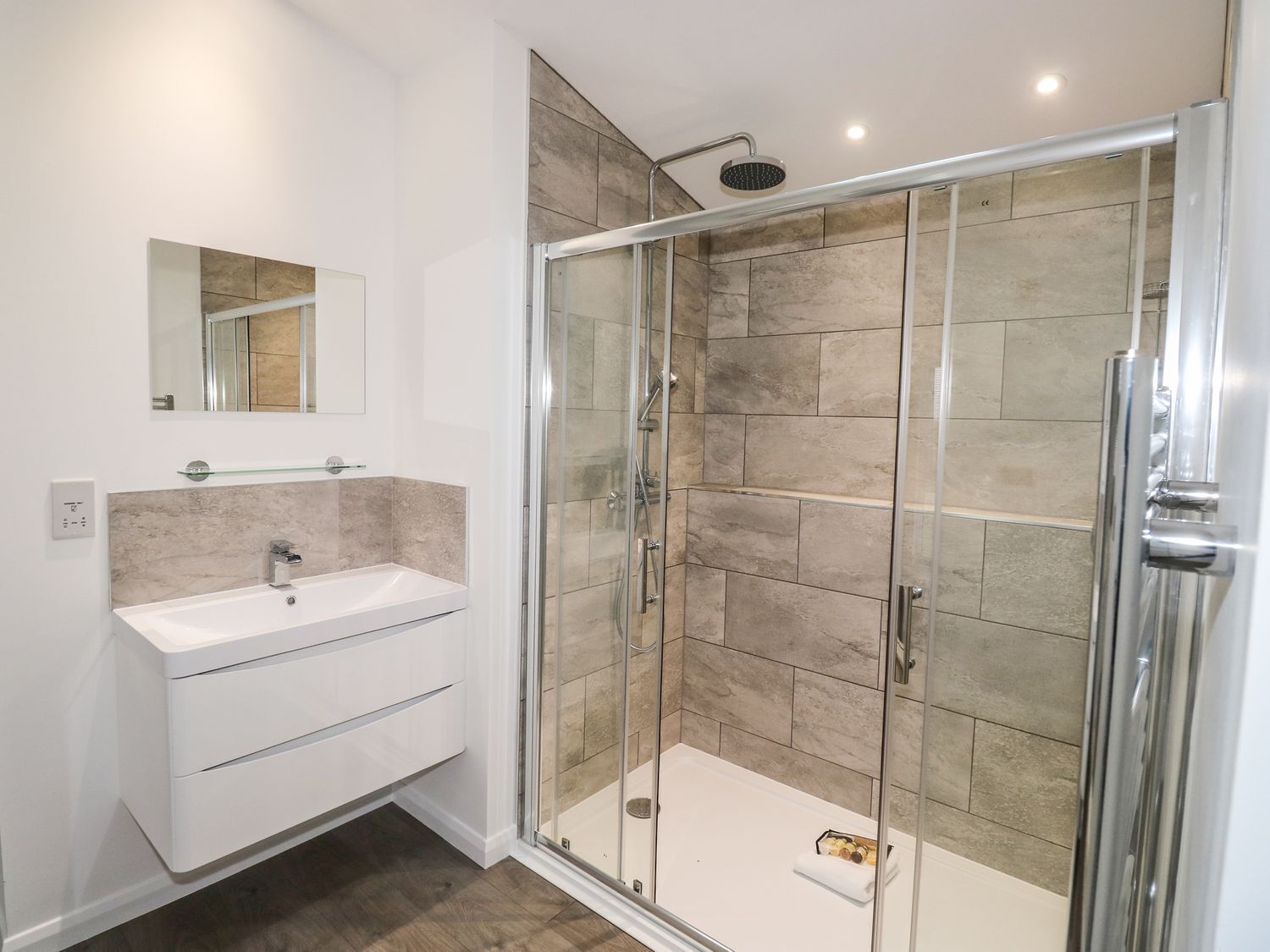 A modern bathroom with a glass-enclosed shower, a white sink with a mirror above it, and beige tiles on the walls.