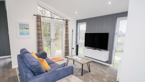 A modern living room with a blue sofa, a small table, a flat-screen TV, and a sliding glass door leading to an outdoor area.