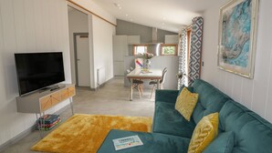 Een moderne woonkamer met een flatscreen-tv, een blauwgroene bank met gele kussens, een geel vloerkleed en een lijst met een abstract schilderij.