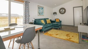 Een moderne woonkamer met een eethoek, een bank met kussens, een vloerkleed en een televisie.