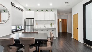 A modern kitchen with white cabinets, a stainless steel refrigerator, and a dining area with a dark wood table and four chairs.
