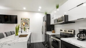 A modern kitchen with a marble countertop, stainless steel appliances, and a flat-screen TV mounted on the wall.