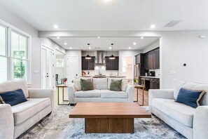 Uma sala de estar moderna com sofá, mesa de centro e cozinha ao fundo.