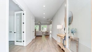 A hallway with wooden flooring, white walls, and a door leading to a room with a ceiling fan. - Beautiful Modern New Home Near Brookhaven Midtown (Atlanta)