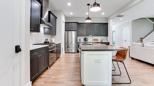 A modern kitchen with dark cabinets, stainless steel appliances, and a central island. - Beautiful Modern New Home Near Brookhaven Midtown (Atlanta)