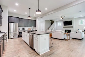 Relax in this open-plan living space featuring a kitchen with stainless steel appliances and a central island, a comfortable sofa set, and a flat-screen TV.